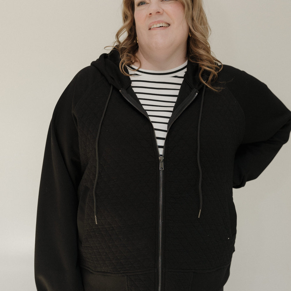 Person wearing a black hoodie over a striped shirt on a plain background