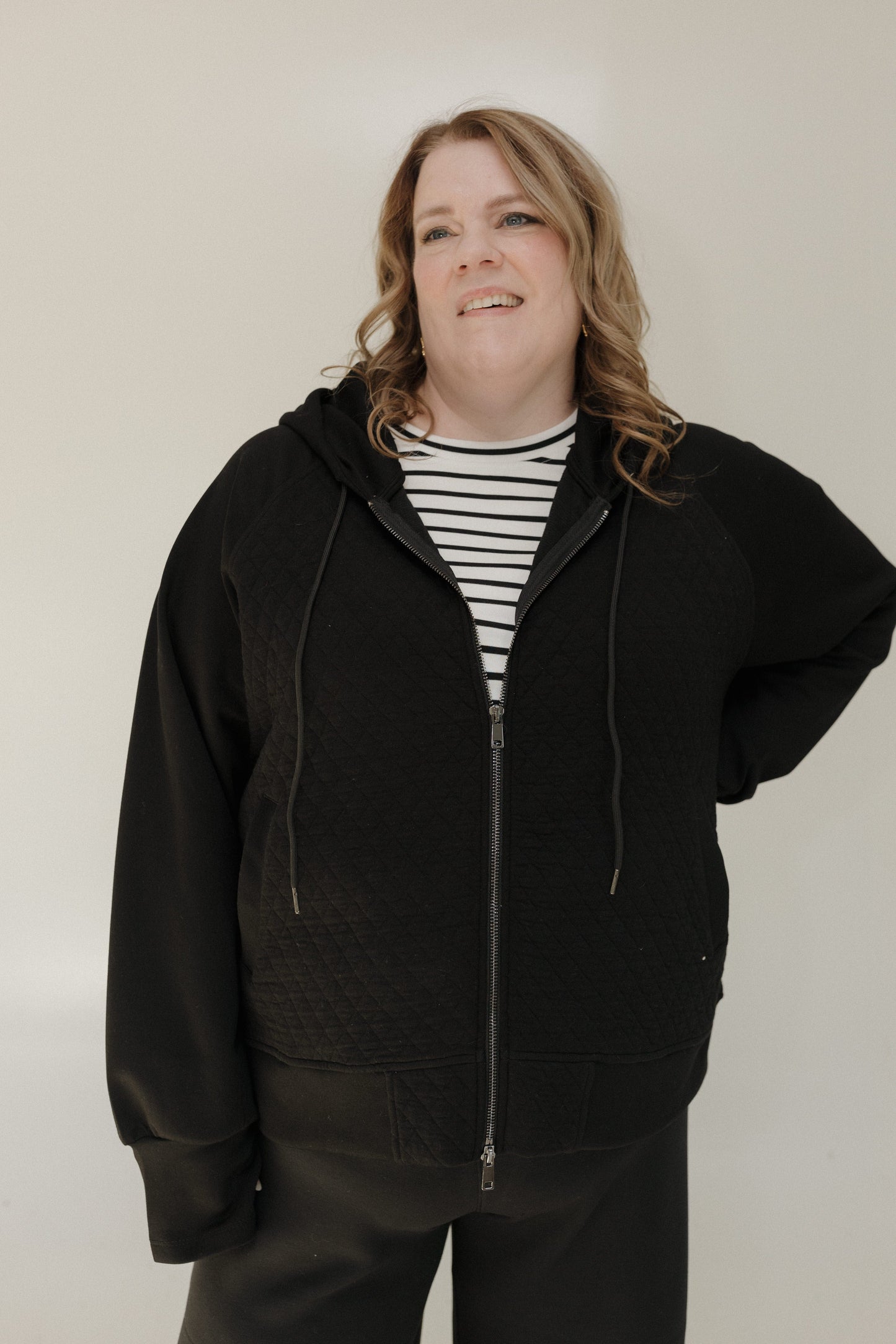 Person wearing a black hoodie over a striped shirt on a plain background