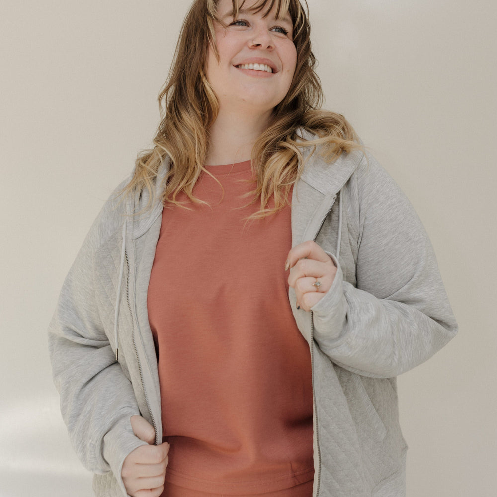 Woman wearing a gray cardigan over a pink top and pants, standing against a plain background.