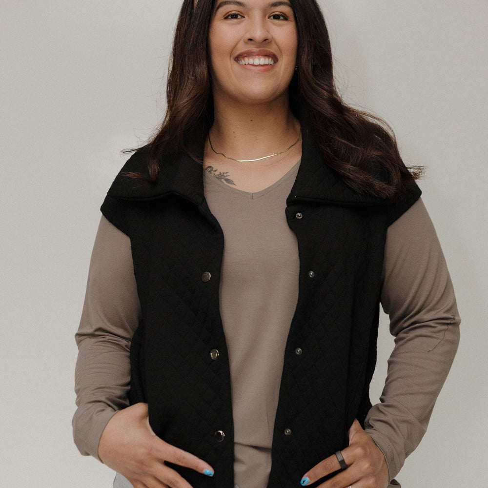 Woman wearing a black vest over a beige shirt with a plain background