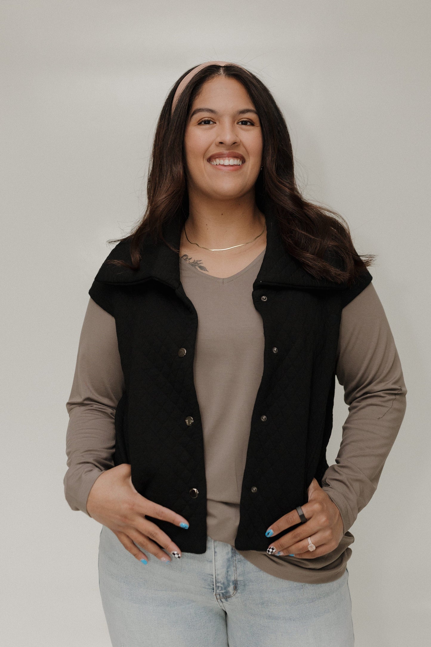 Woman wearing a black vest over a beige shirt with a plain background