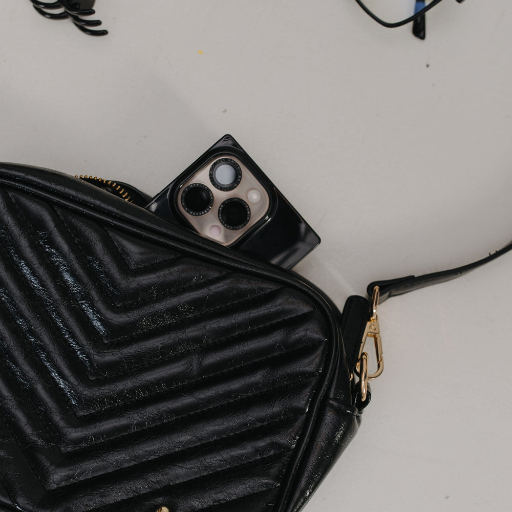 Black quilted handbag with a phone, glasses, and small black spider toy on a light gray background