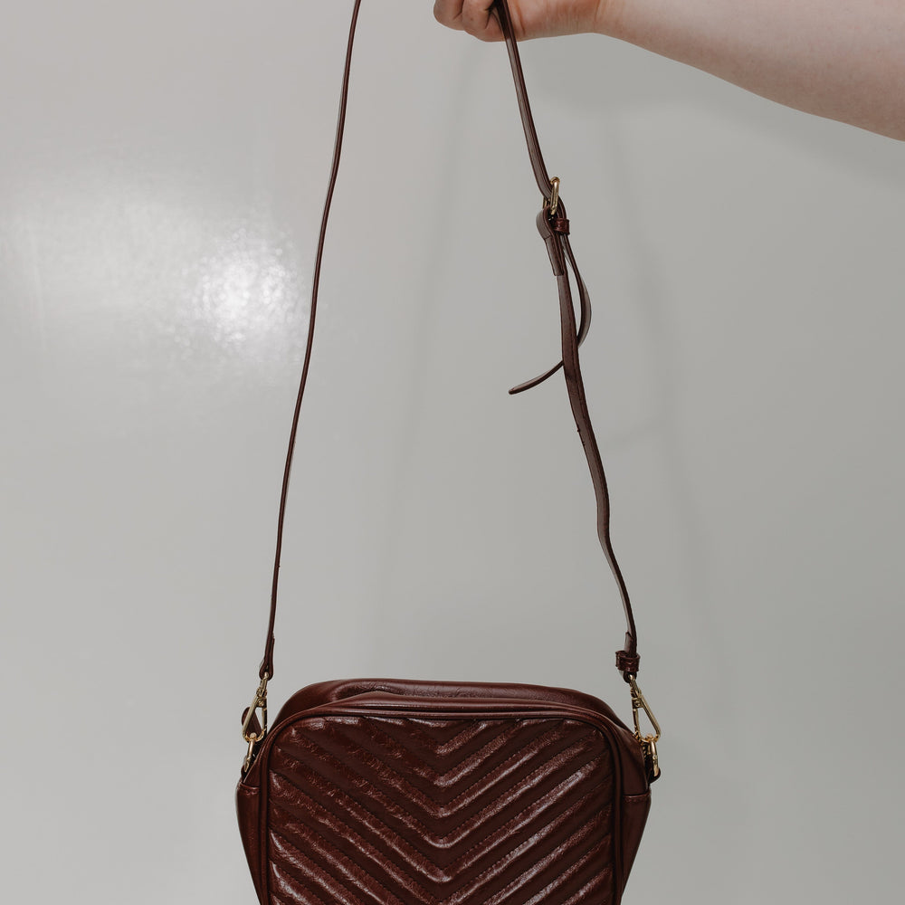 Burgundy quilted handbag held by a hand against a plain background