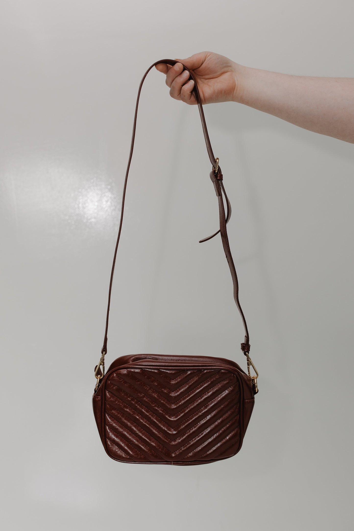 Burgundy quilted handbag held by a hand against a plain background