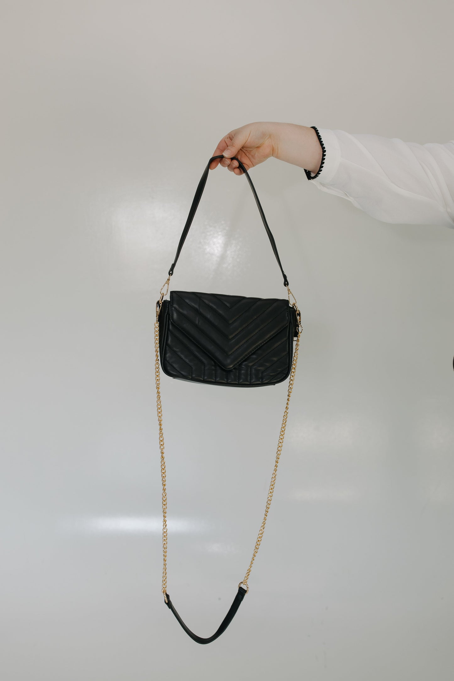 Black quilted handbag with a gold chain strap held by a person against a light gray background