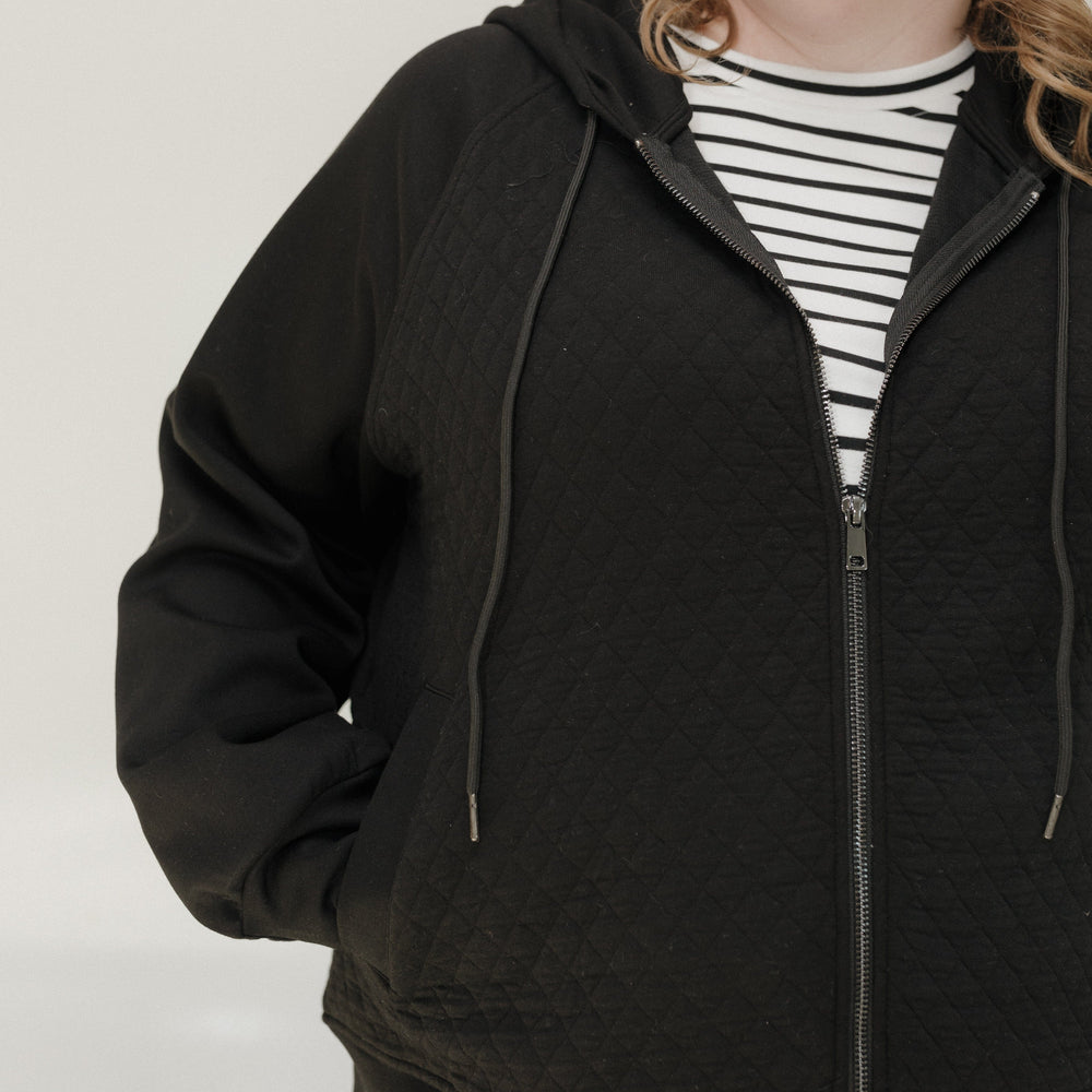 Person wearing a black quilted jacket over a striped shirt on a plain background