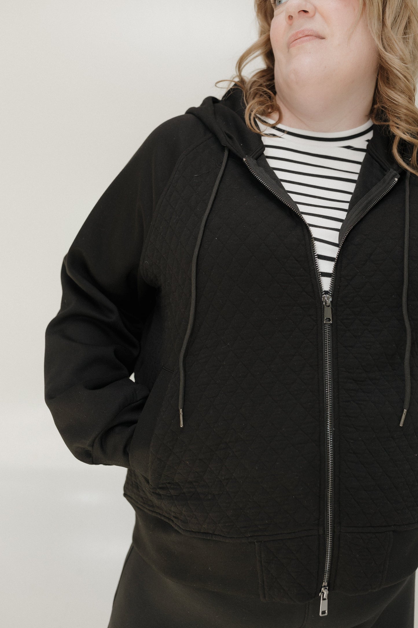 Person wearing a black quilted jacket over a striped shirt on a plain background