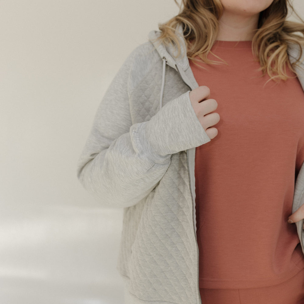 Woman wearing a gray hoodie and pink pants against a plain background