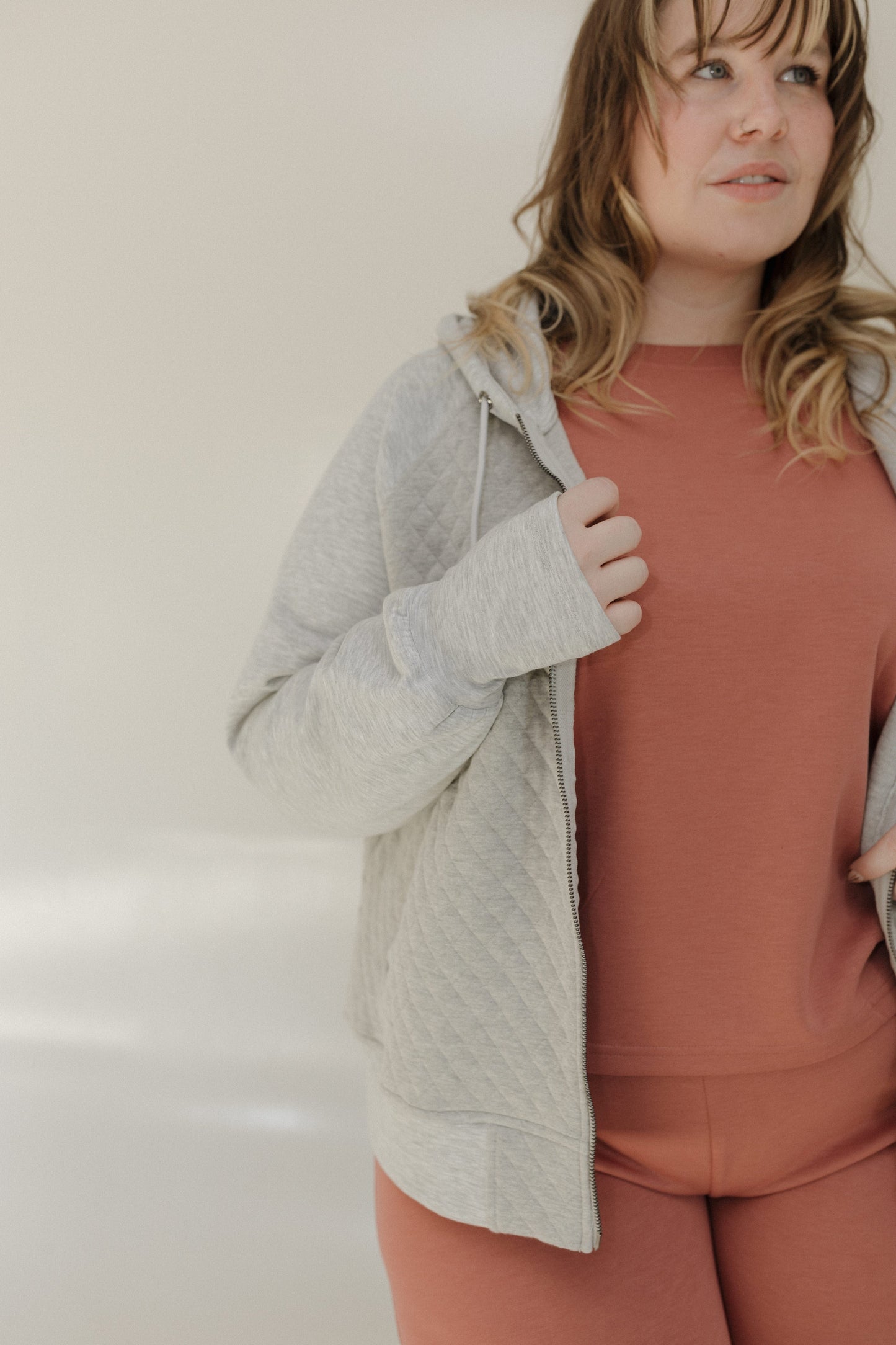 Woman wearing a gray hoodie and pink pants against a plain background
