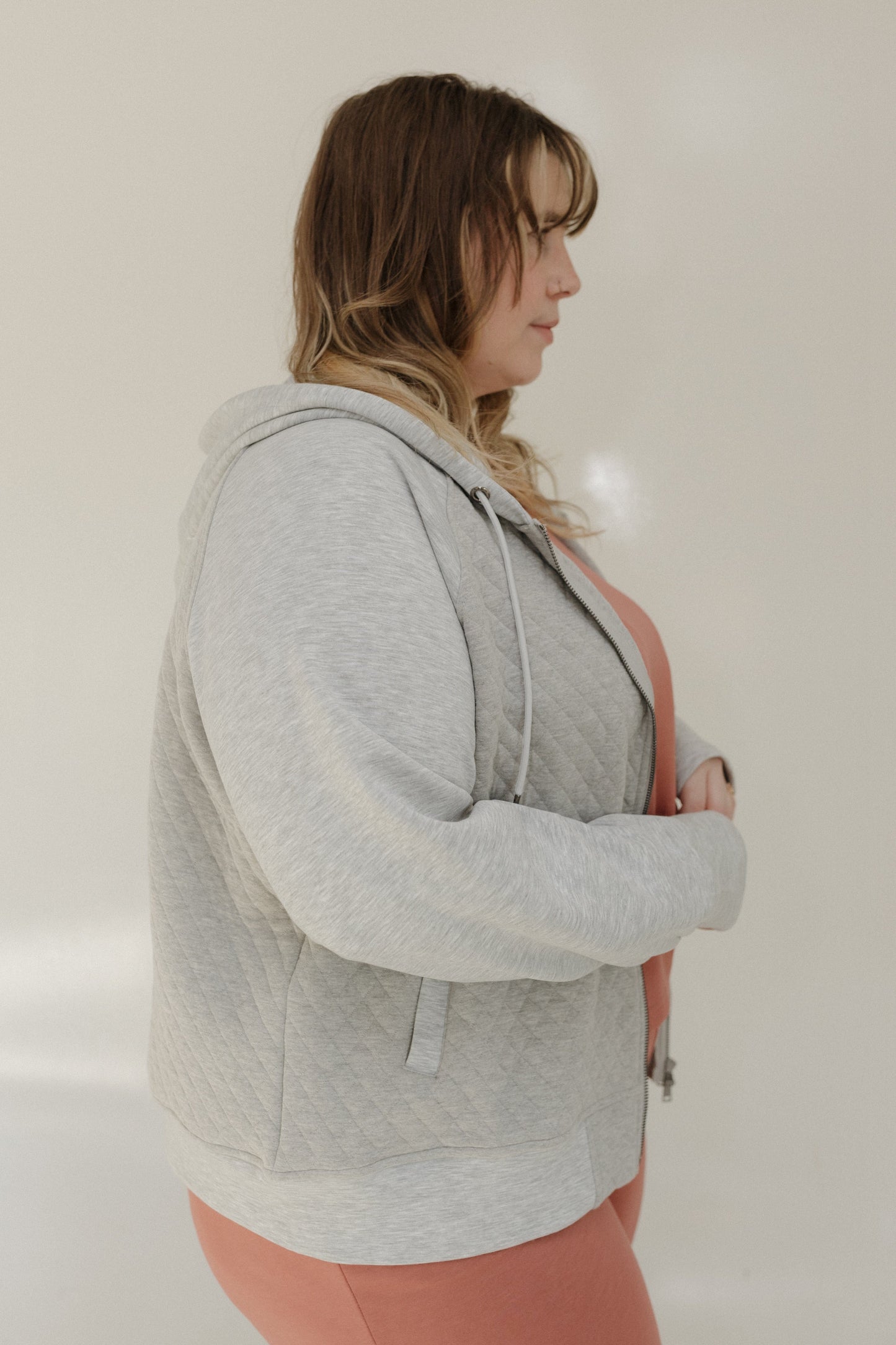 Woman wearing a gray hoodie and pink pants against a plain background