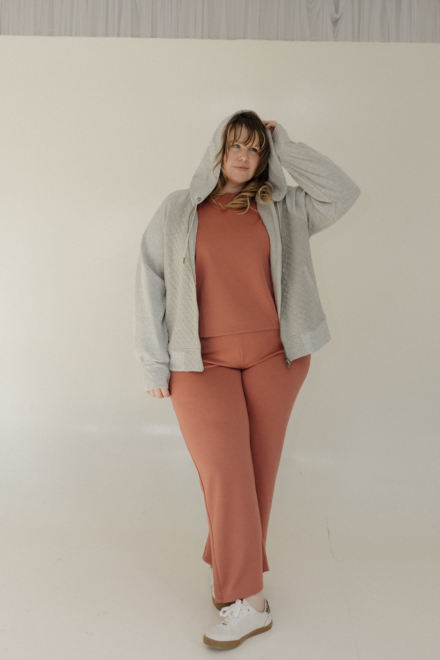 Person wearing a gray jacket and pink pants against a plain background