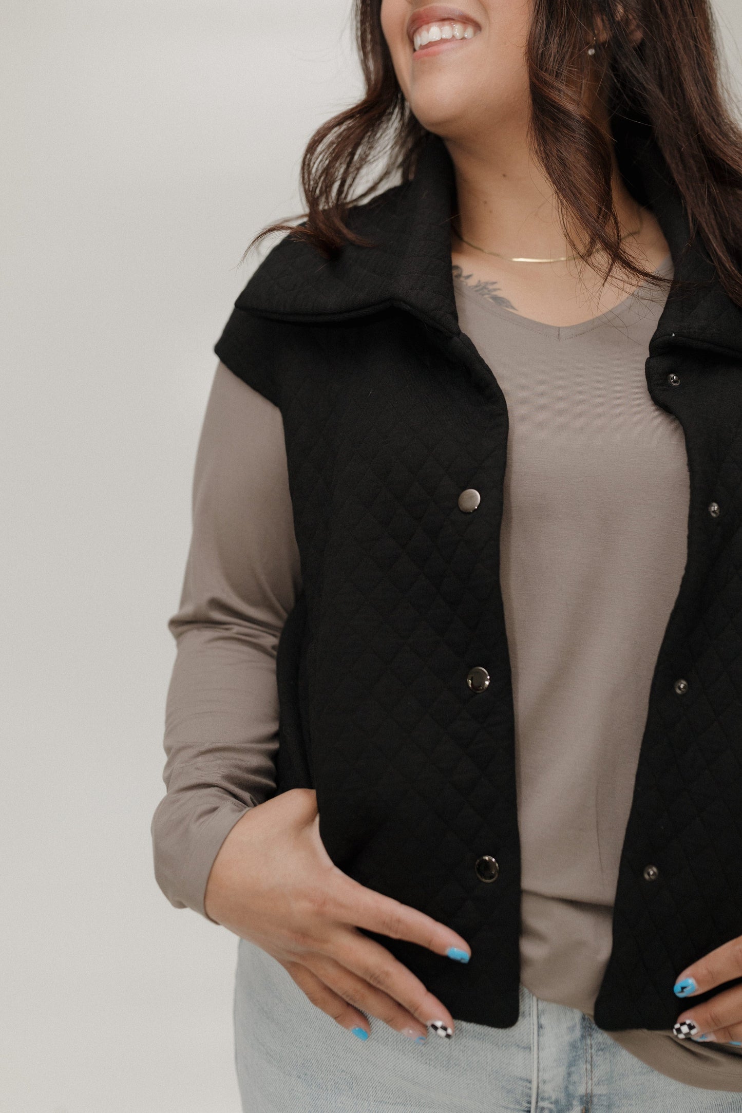Woman wearing a black quilted vest over a beige top against a plain background