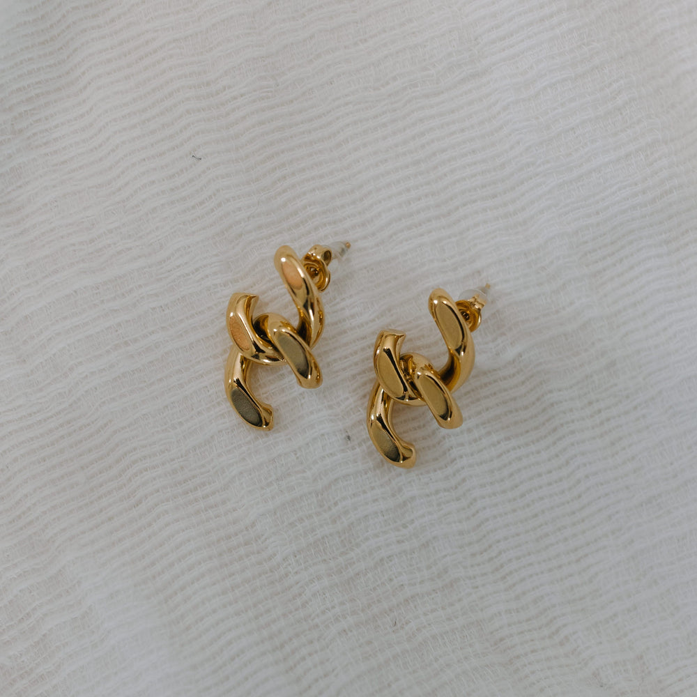 Gold chain-style earrings on a light gray fabric background