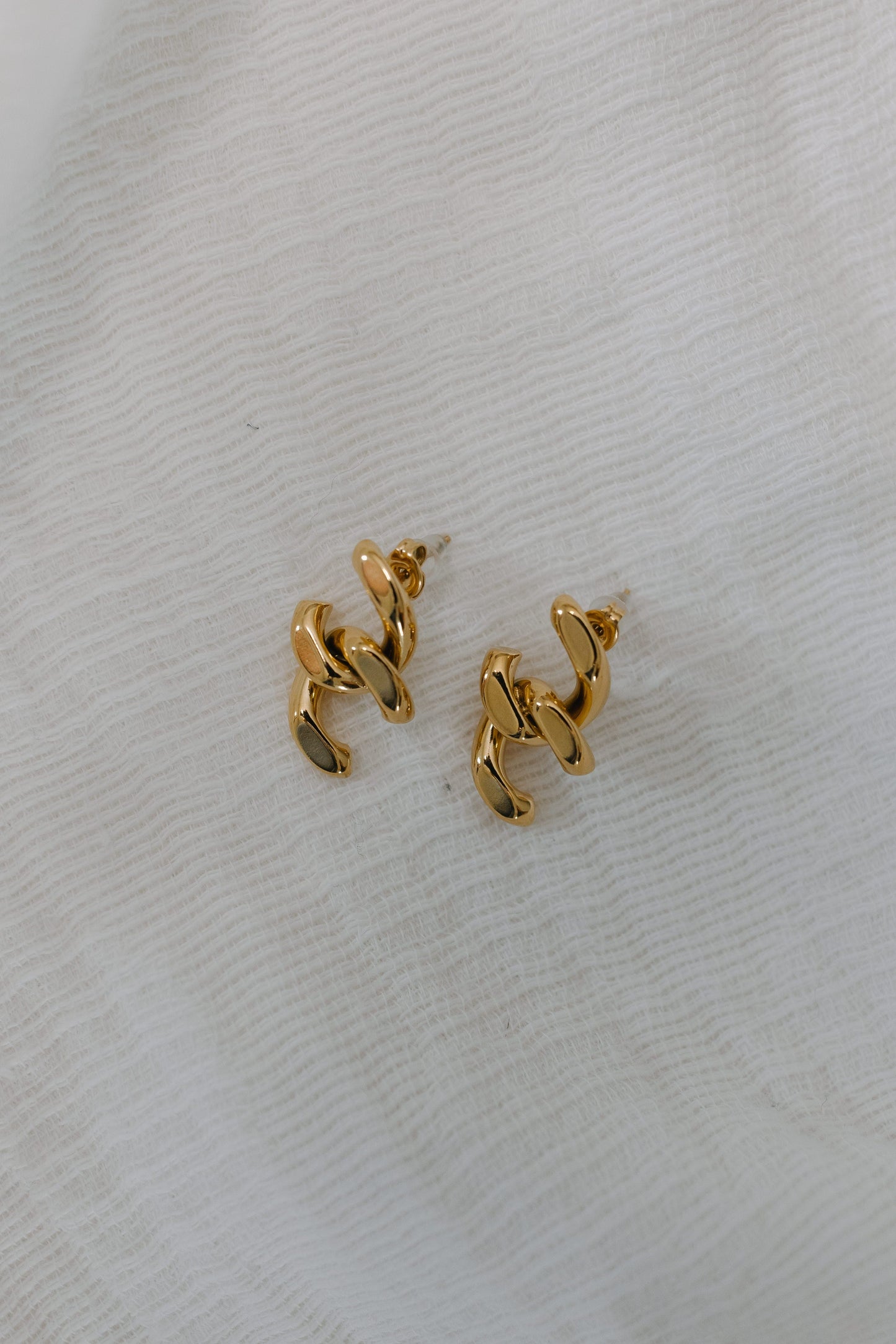 Gold chain-style earrings on a light gray fabric background
