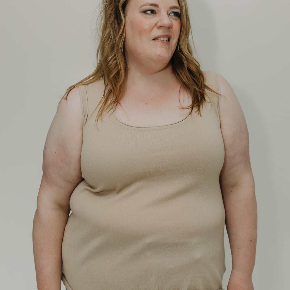 Woman wearing a beige tank top and light blue jeans against a plain background