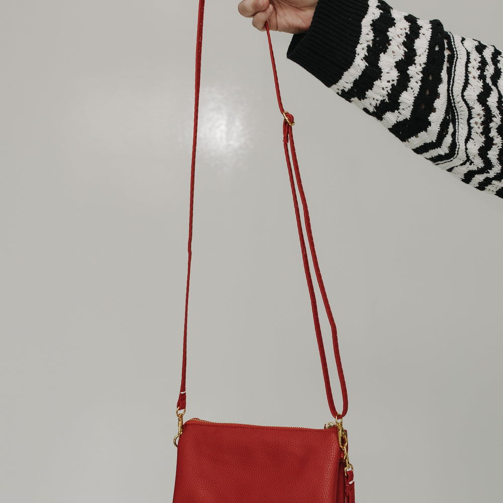 Red handbag held by a person wearing a black and white striped sweater against a plain background