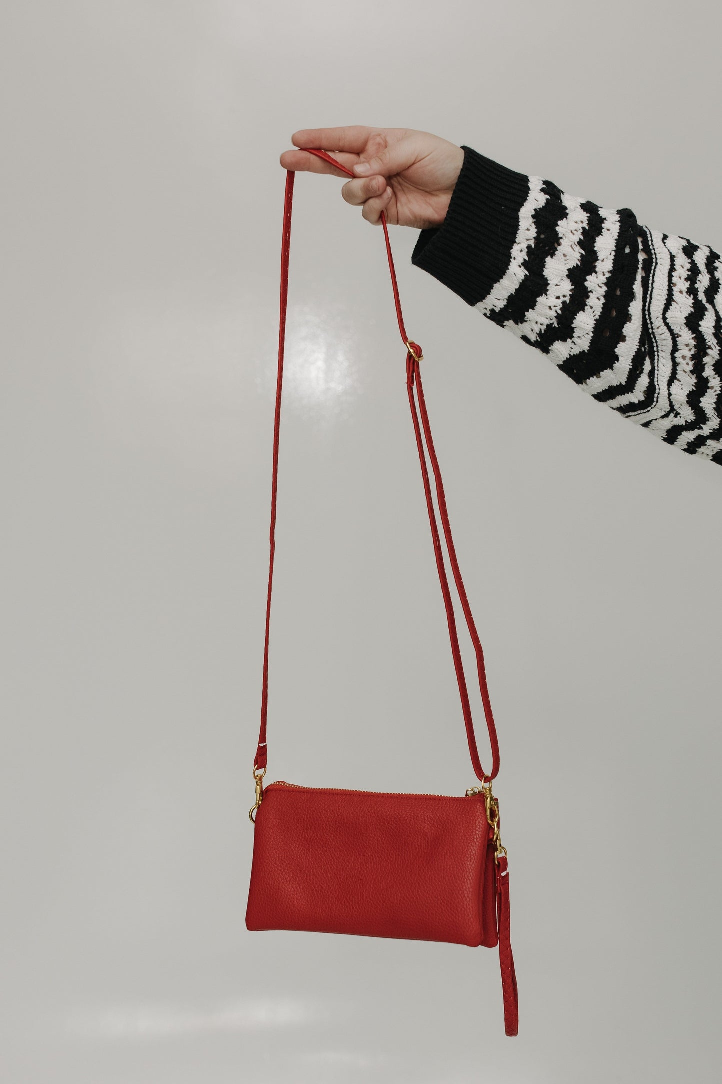 Red handbag held by a person wearing a black and white striped sweater against a plain background