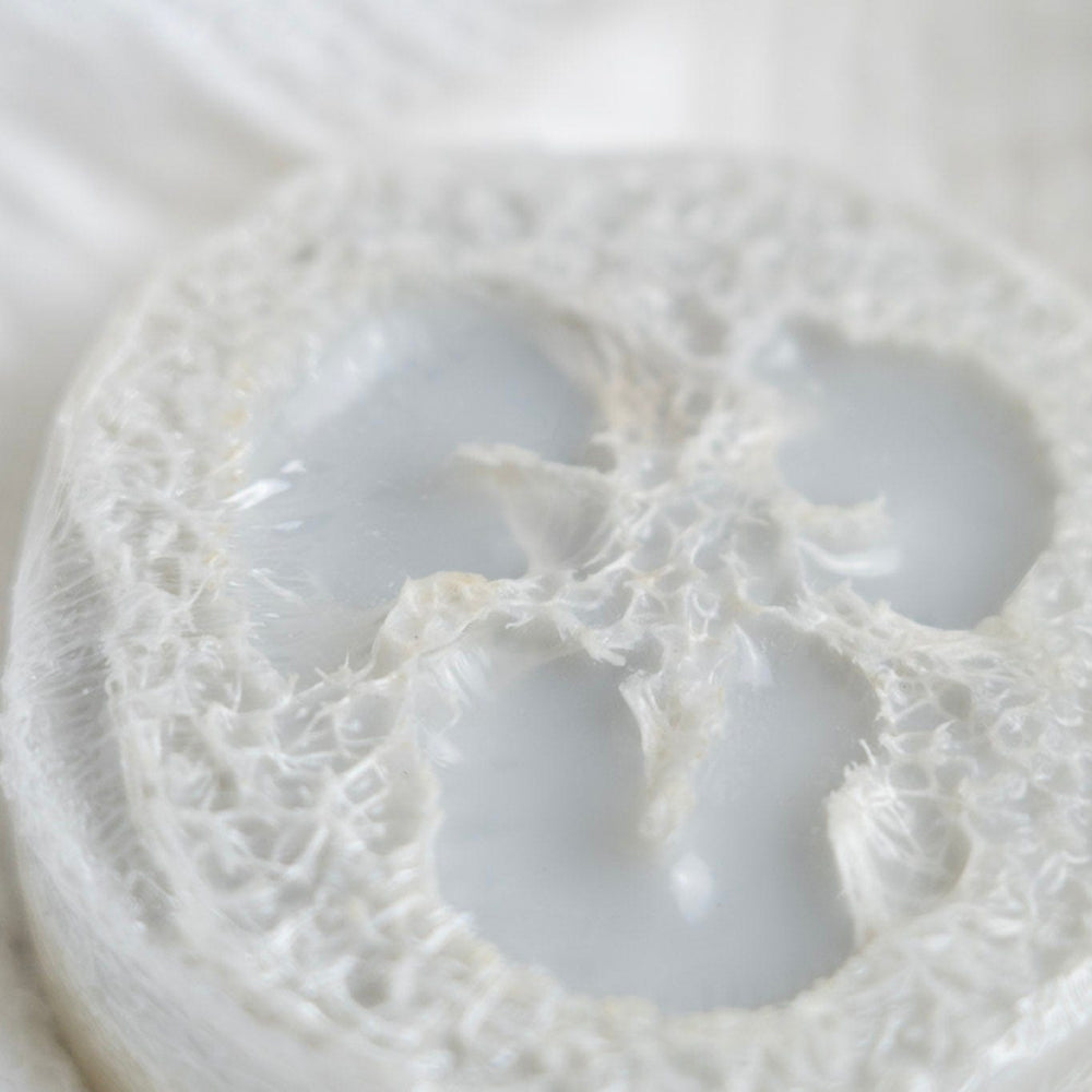 Close-up of a loofah soap on a  textured white fabric with a circular pattern