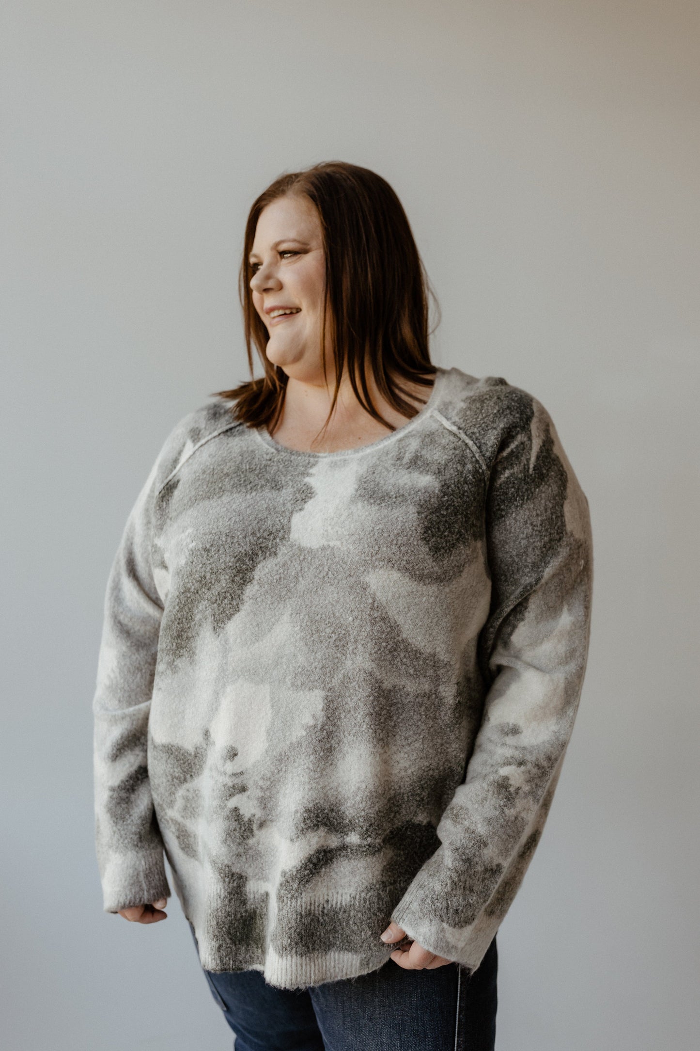 A person wearing a versatile gray and white sweater stands against a plain background, smiling and looking to the side.