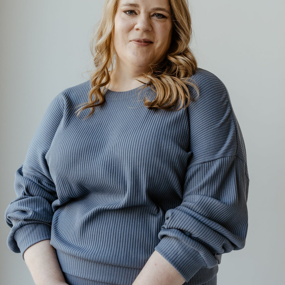 A person with long, wavy hair is wearing the Ribbed Cropped Sweater in Adrift by Mikarose, standing against a plain background and looking directly at the camera.