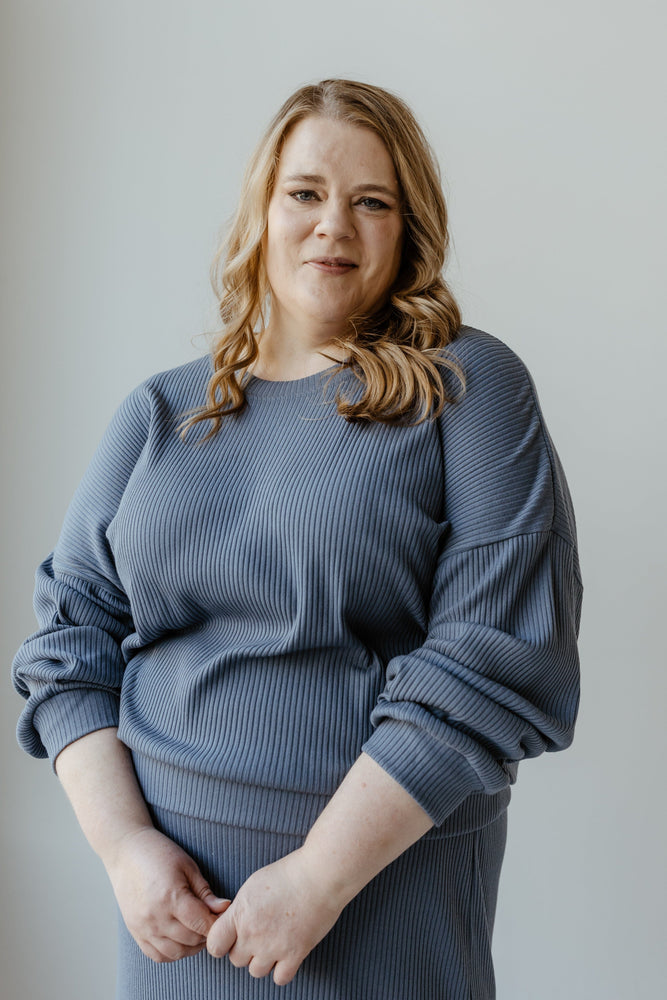 A person with long, wavy hair is wearing the Ribbed Cropped Sweater in Adrift by Mikarose, standing against a plain background and looking directly at the camera.