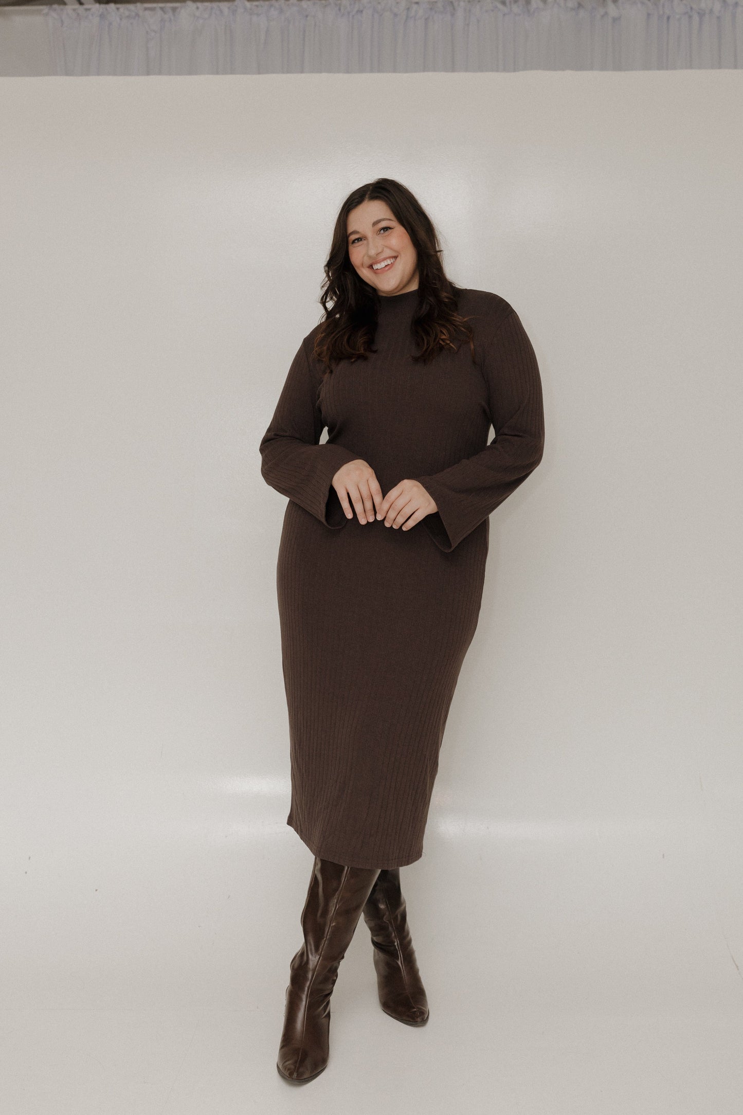 Woman wearing a brown dress and boots against a white background