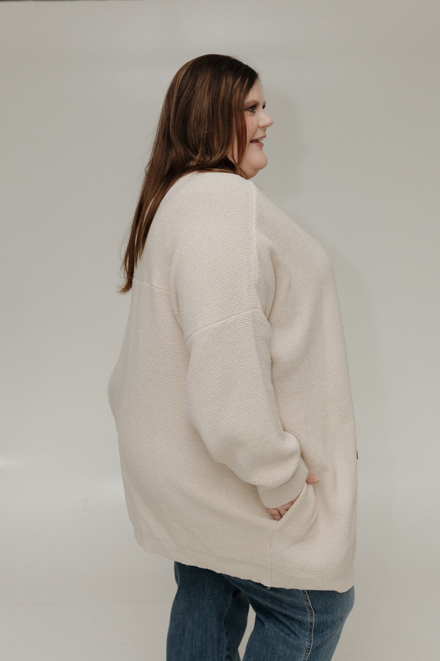 Person wearing a beige sweater and blue jeans against a plain background