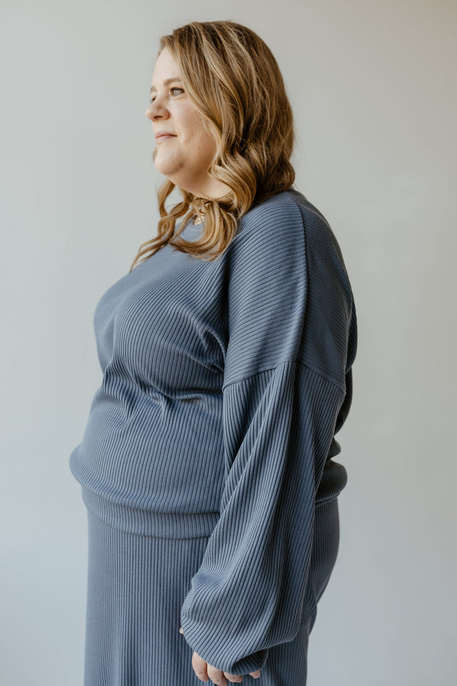 A person with long hair elegantly wears a ribbed, long-sleeve dress paired with the RIBBED CROPPED SWEATER IN ADRIFT by Mikarose, looking to the side against a plain background.