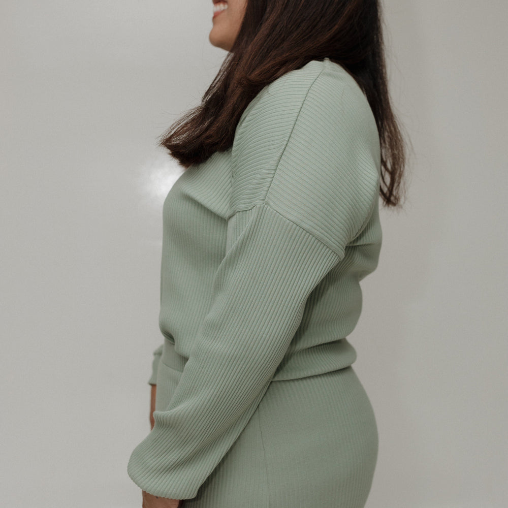 Woman wearing a light green sweater and skirt set against a plain background