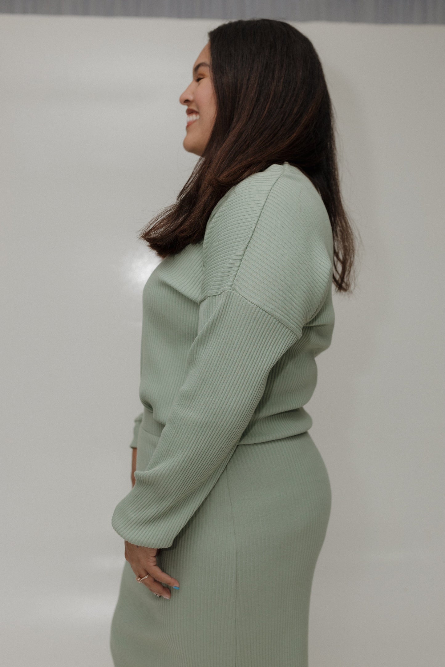 Woman wearing a light green sweater and skirt set against a plain background