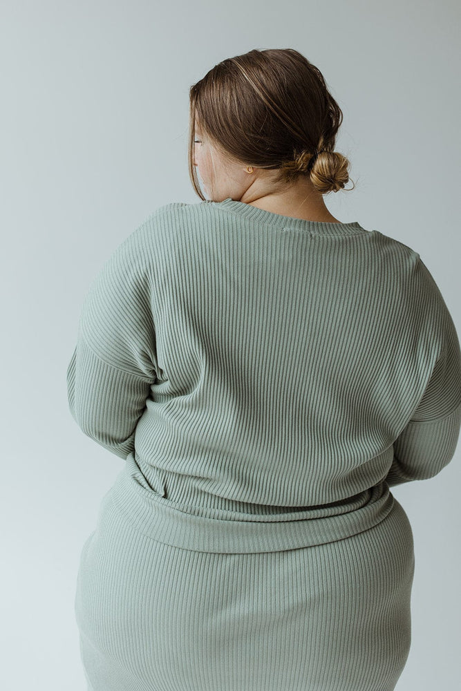 A person wearing the Mikarose Ribbed Cropped Sweater in Faded Jade, featuring dolman sleeves, is viewed from behind against a plain background.