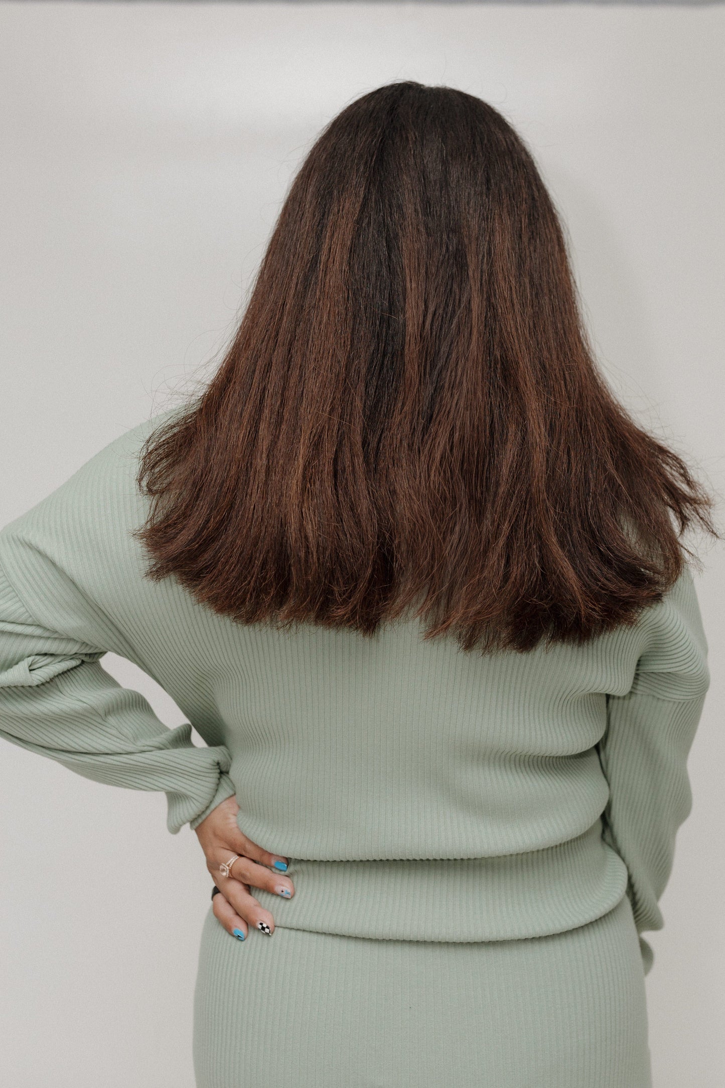 Person wearing a light green outfit with long hair, standing against a plain background