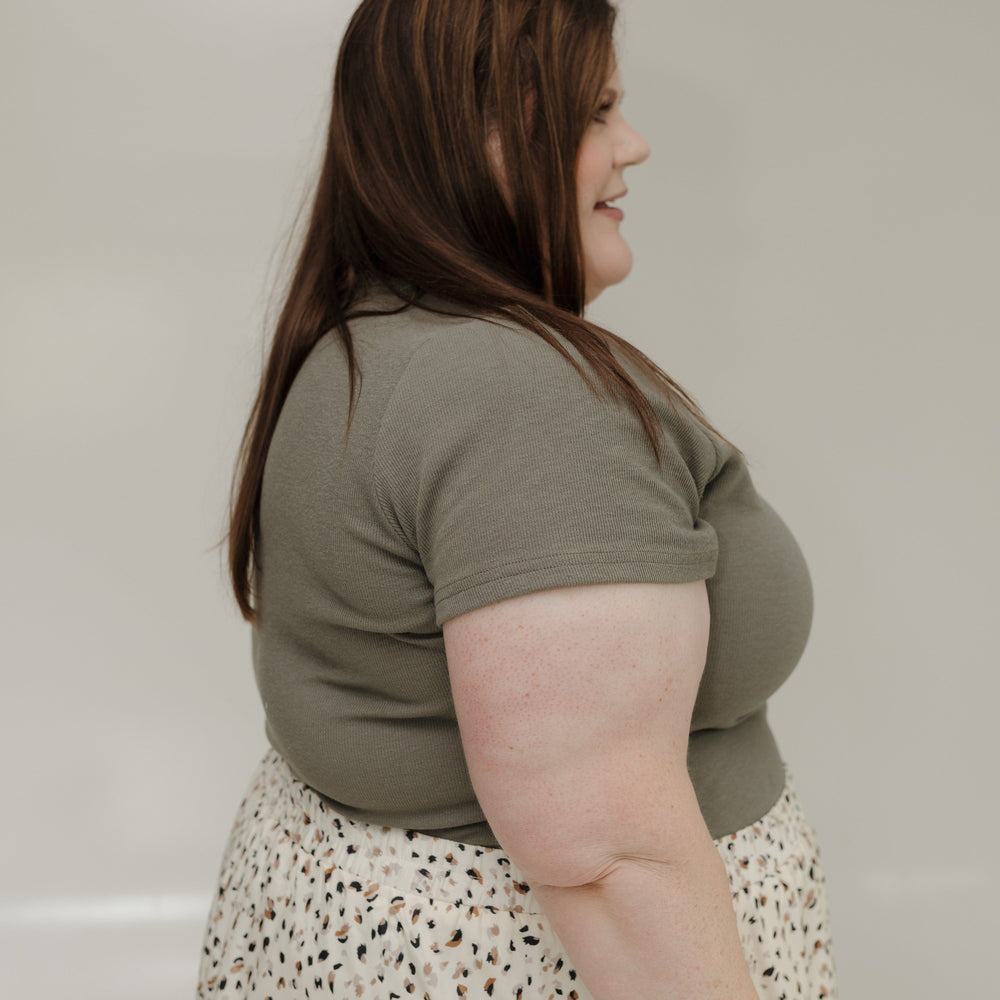 Woman wearing a green shirt and patterned skirt against a plain background