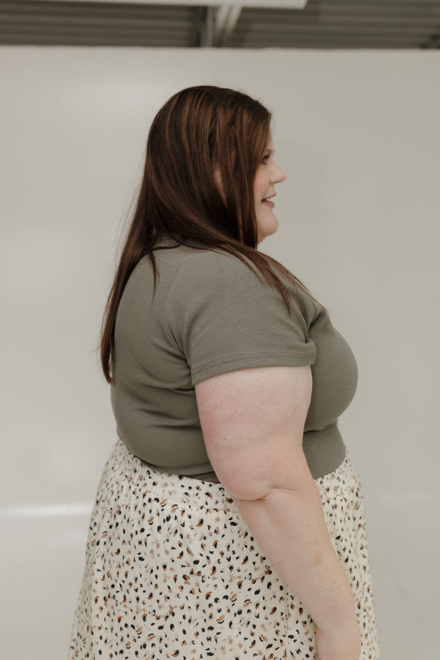 Woman wearing a green shirt and patterned skirt against a plain background