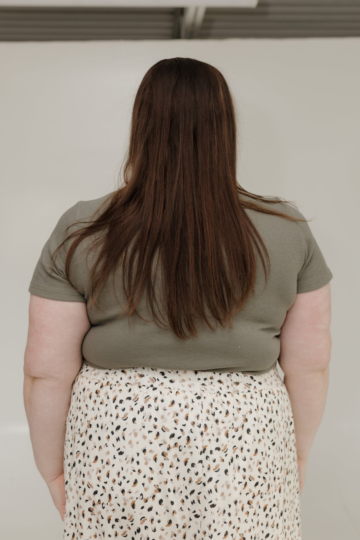 Person wearing a green shirt and patterned skirt against a plain background