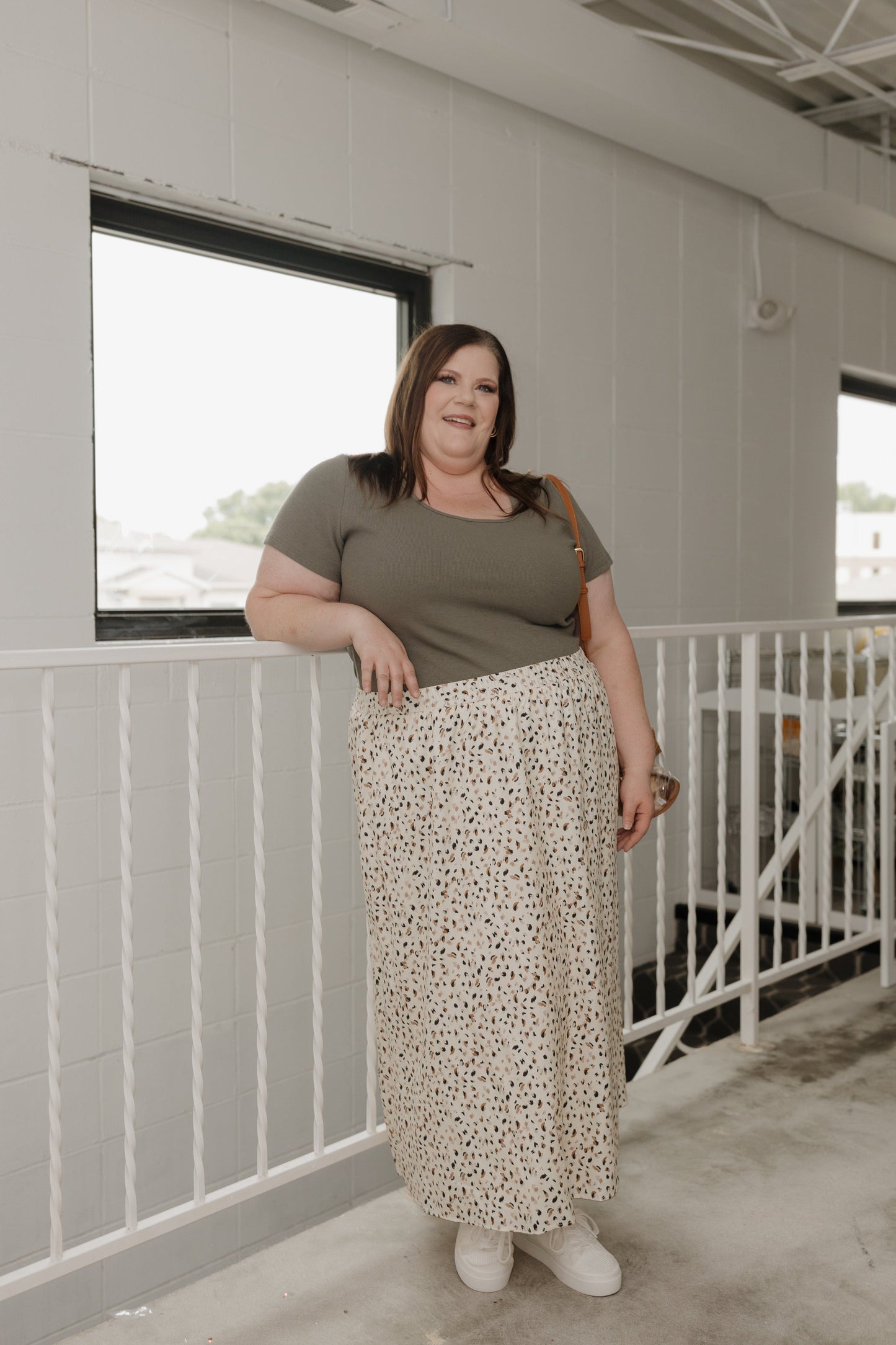 Woman standing indoors wearing a green top and patterned skirt.