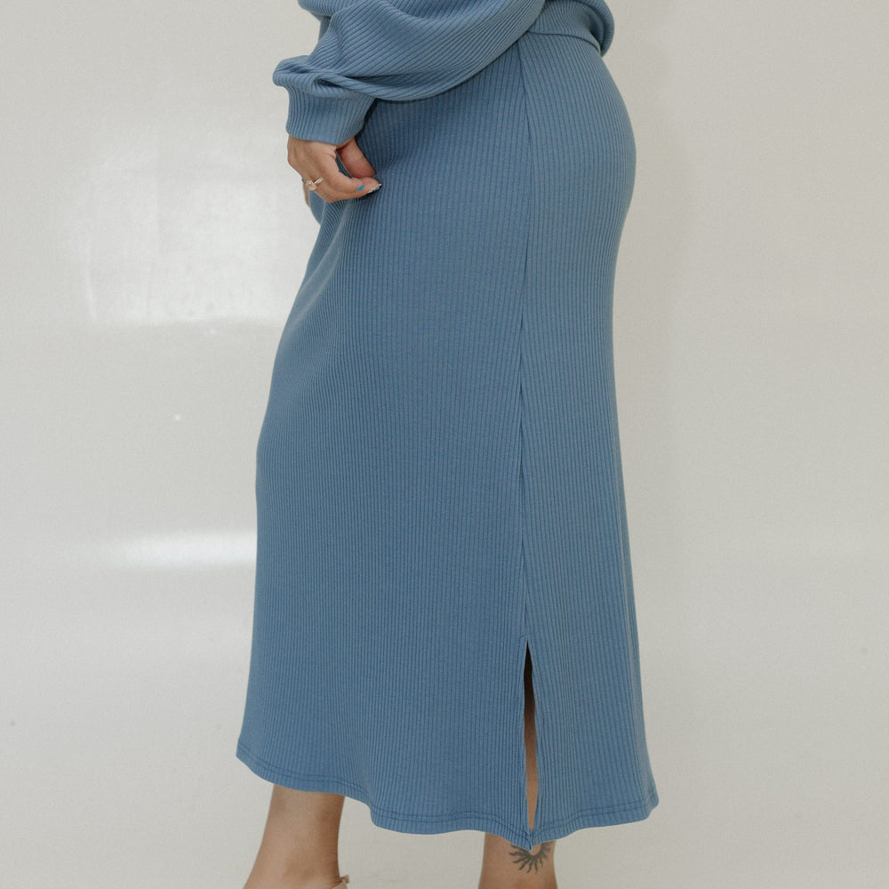 Person wearing a blue ribbed sweater and skirt set with beige heels on a white background