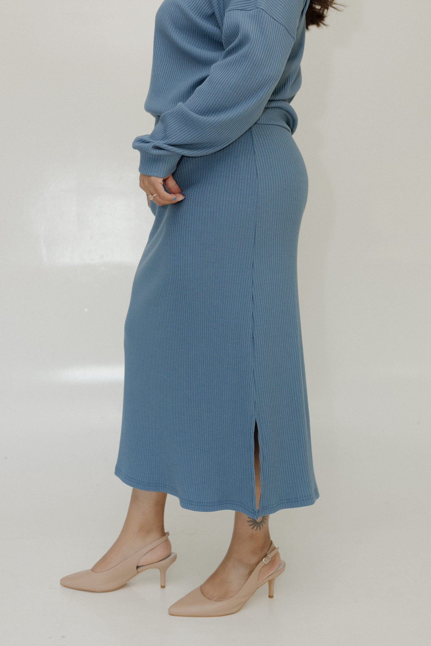 Person wearing a blue ribbed sweater and skirt set with beige heels on a white background