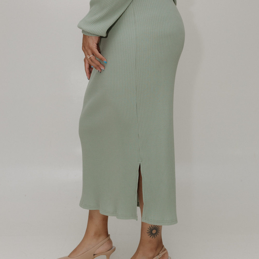 Person wearing a green ribbed sweater and skirt set with beige heels on a white background