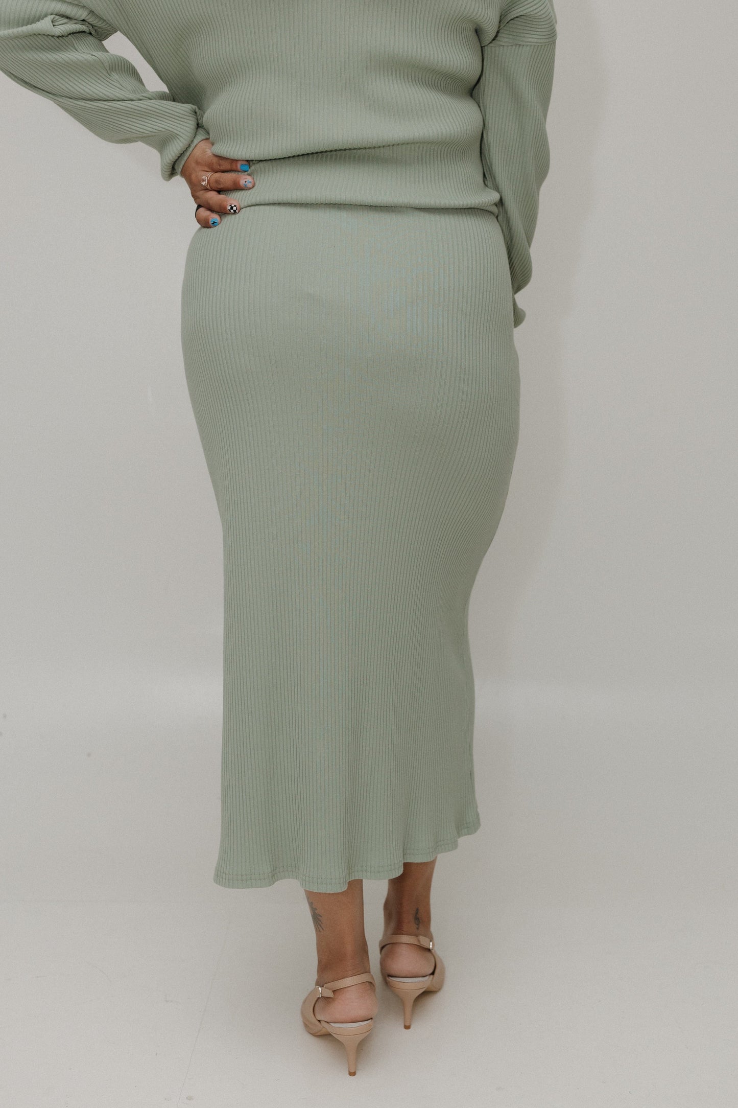 Person wearing a green ribbed sweater and skirt set on a plain background