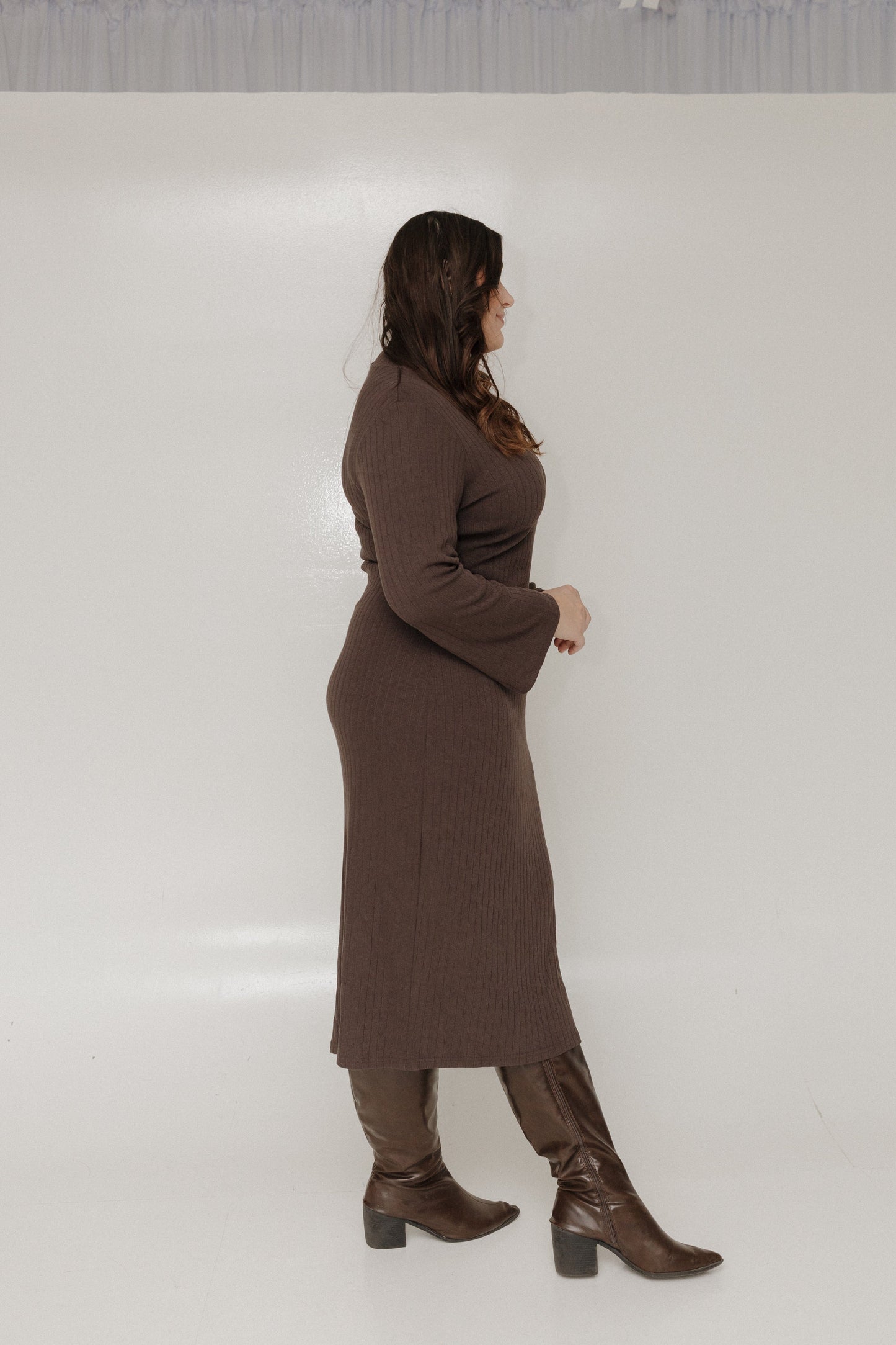 Woman wearing a brown dress and boots against a white background