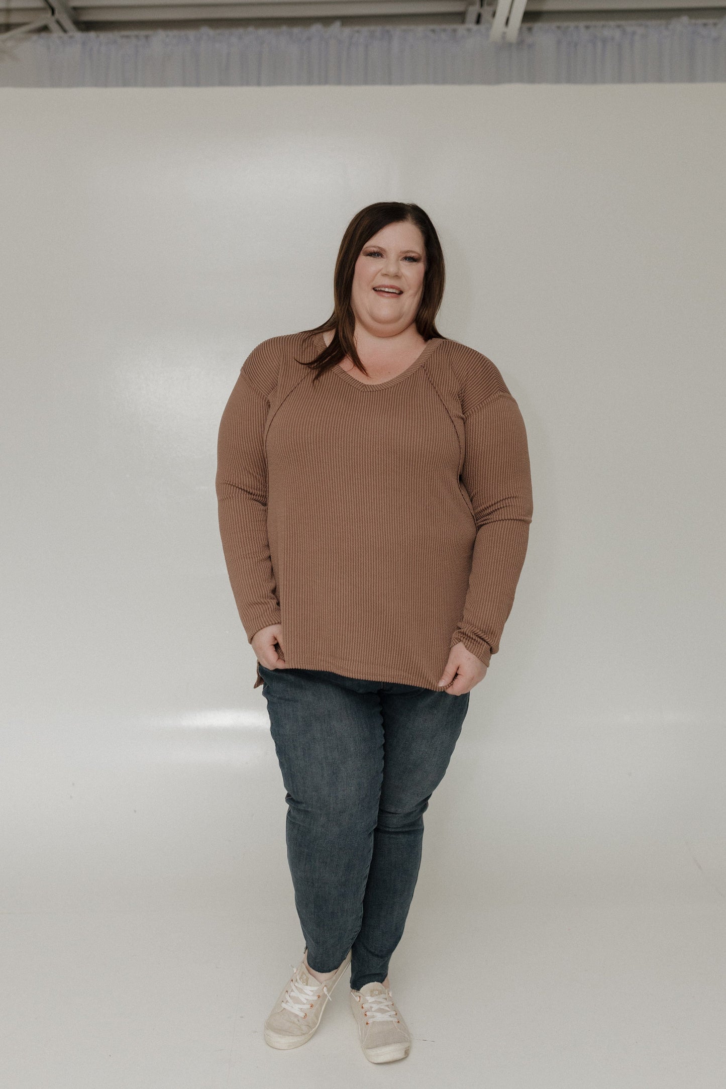 Person wearing a brown tee and jeans standing against a white background