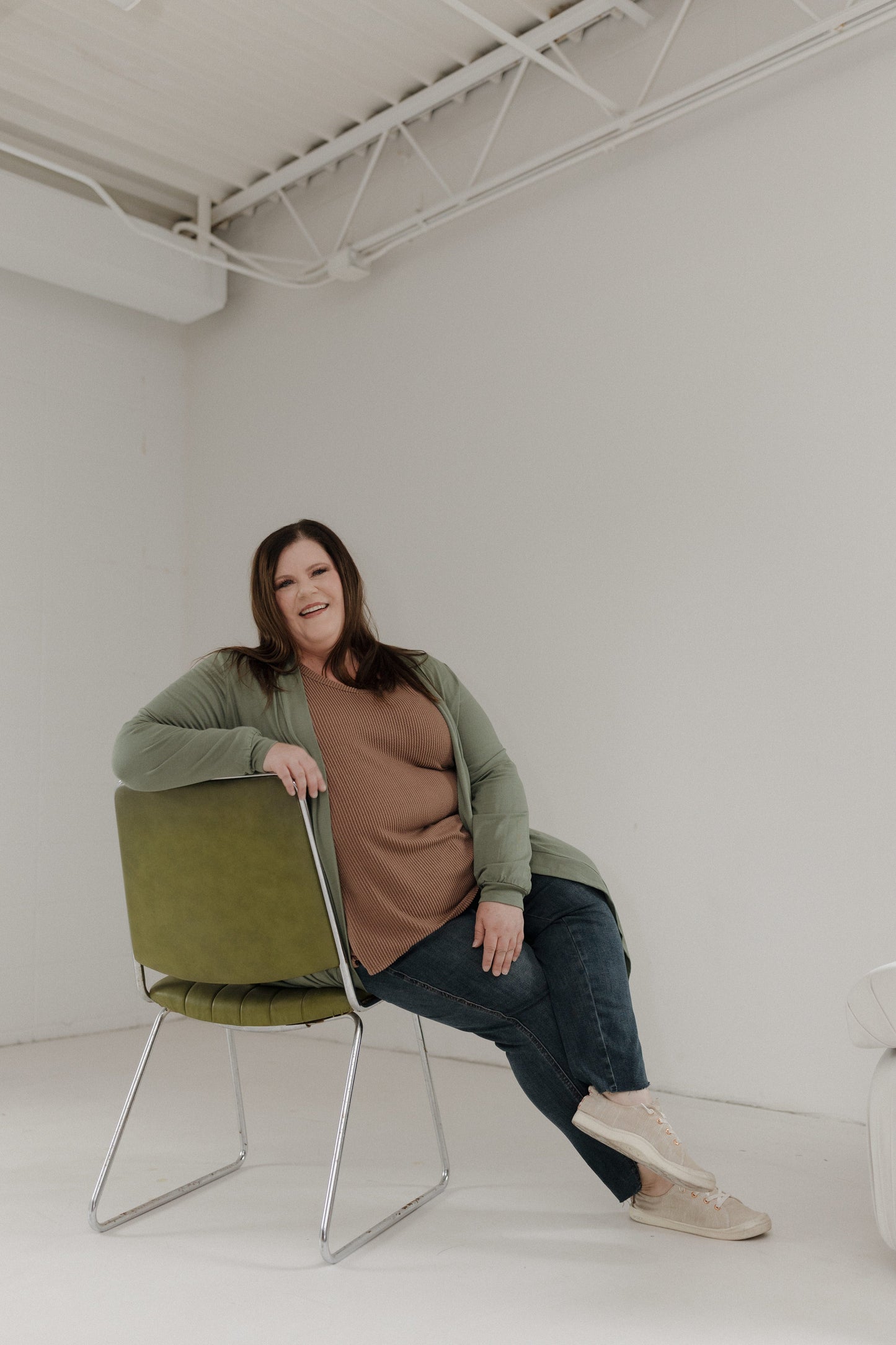 Woman sitting on a green chair in a minimalistic room.