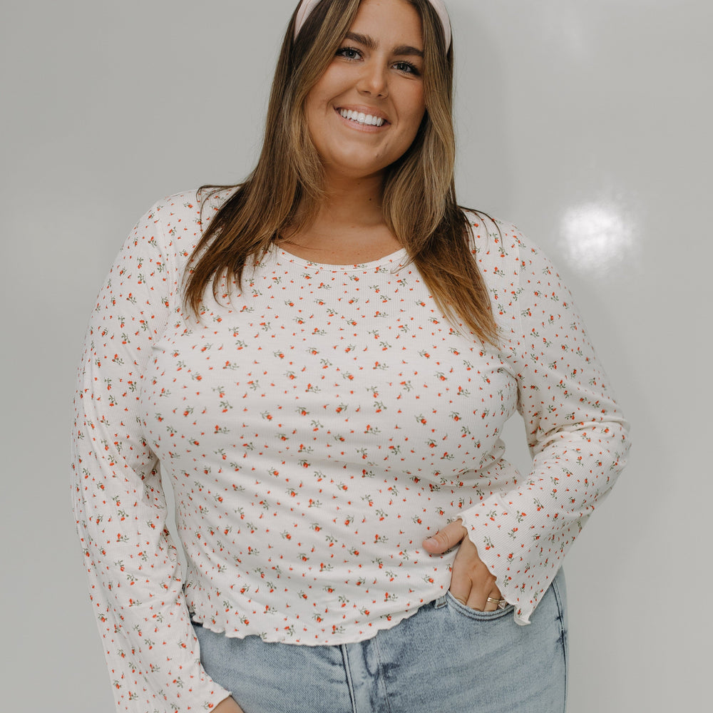 Woman wearing a floral blouse and light blue jeans against a plain background