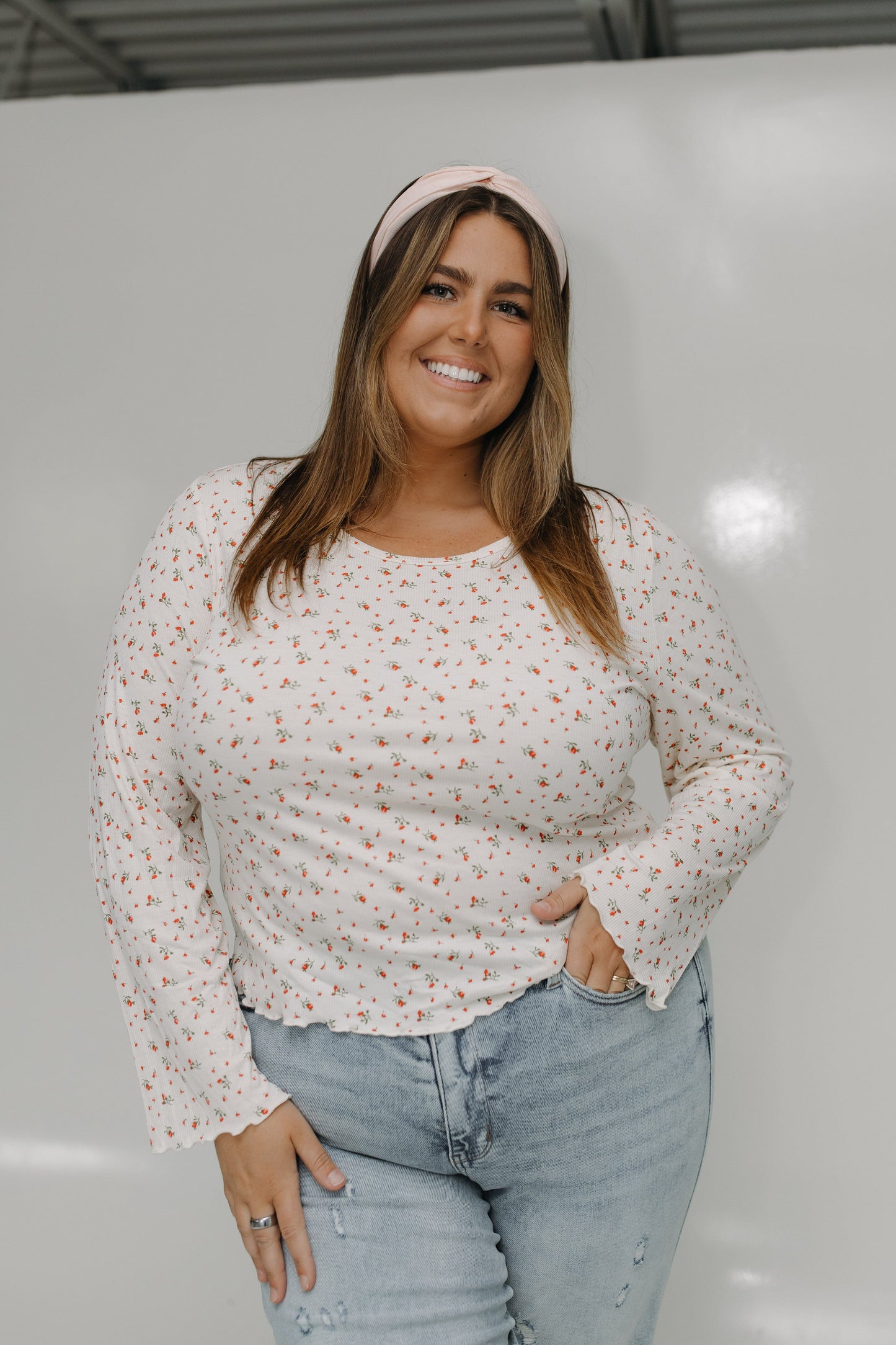 Woman wearing a floral blouse and light blue jeans against a plain background
