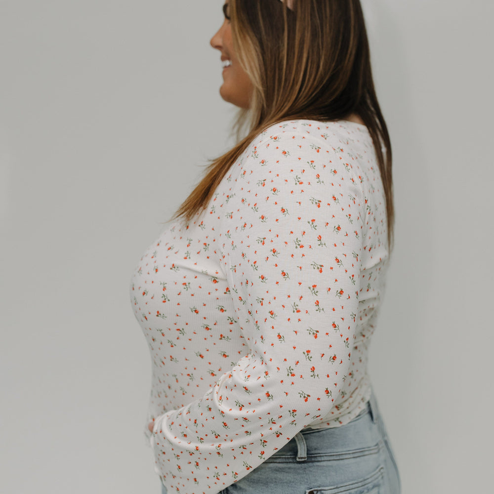 Woman wearing a white floral blouse and light blue jeans against a plain background