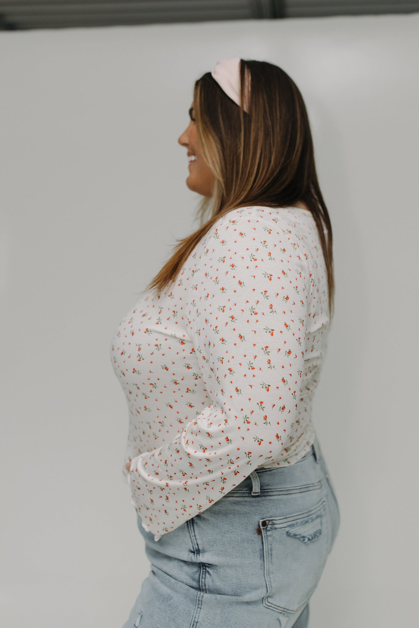 Woman wearing a white floral blouse and light blue jeans against a plain background