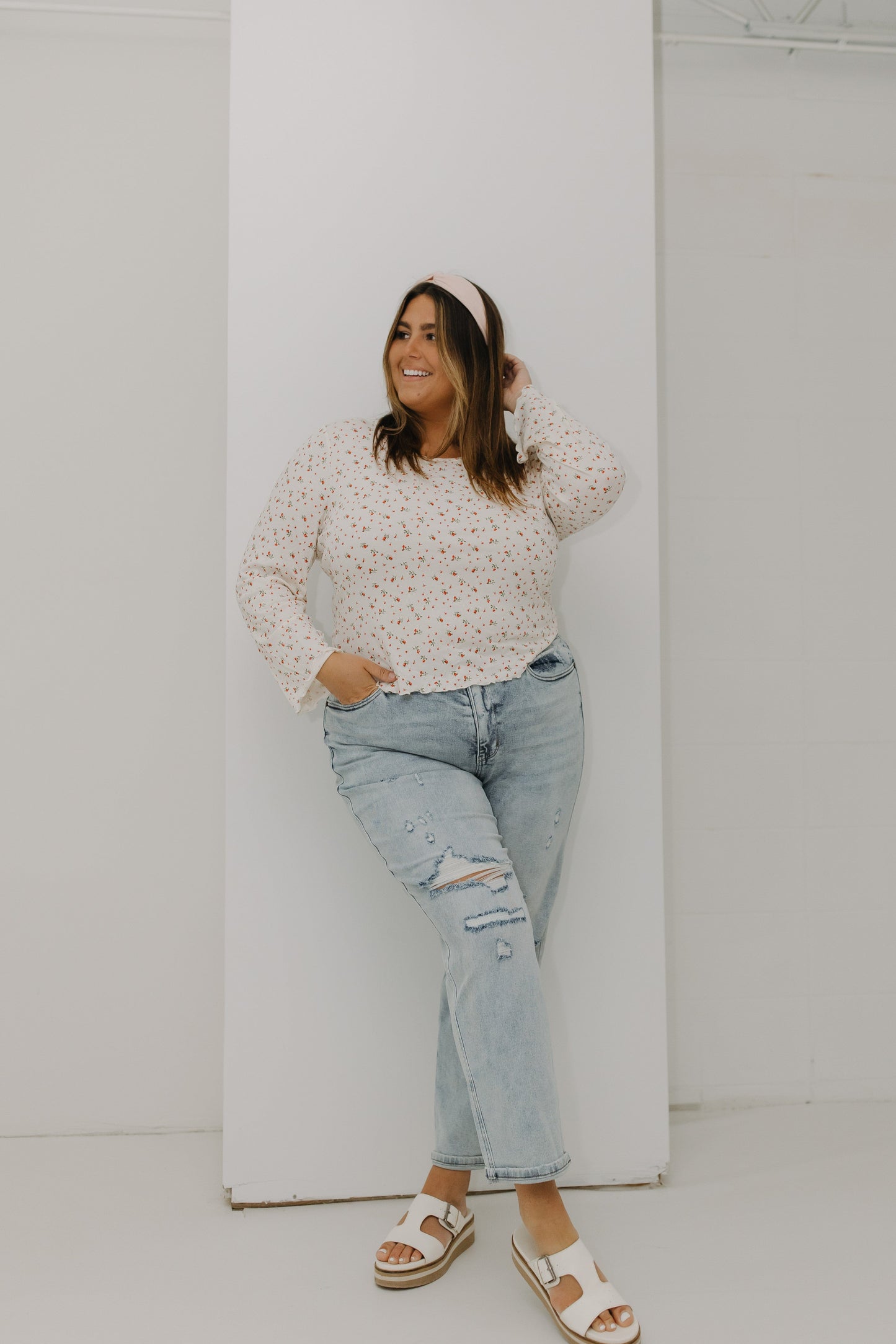 Woman wearing a floral top and ripped jeans against a white wall
