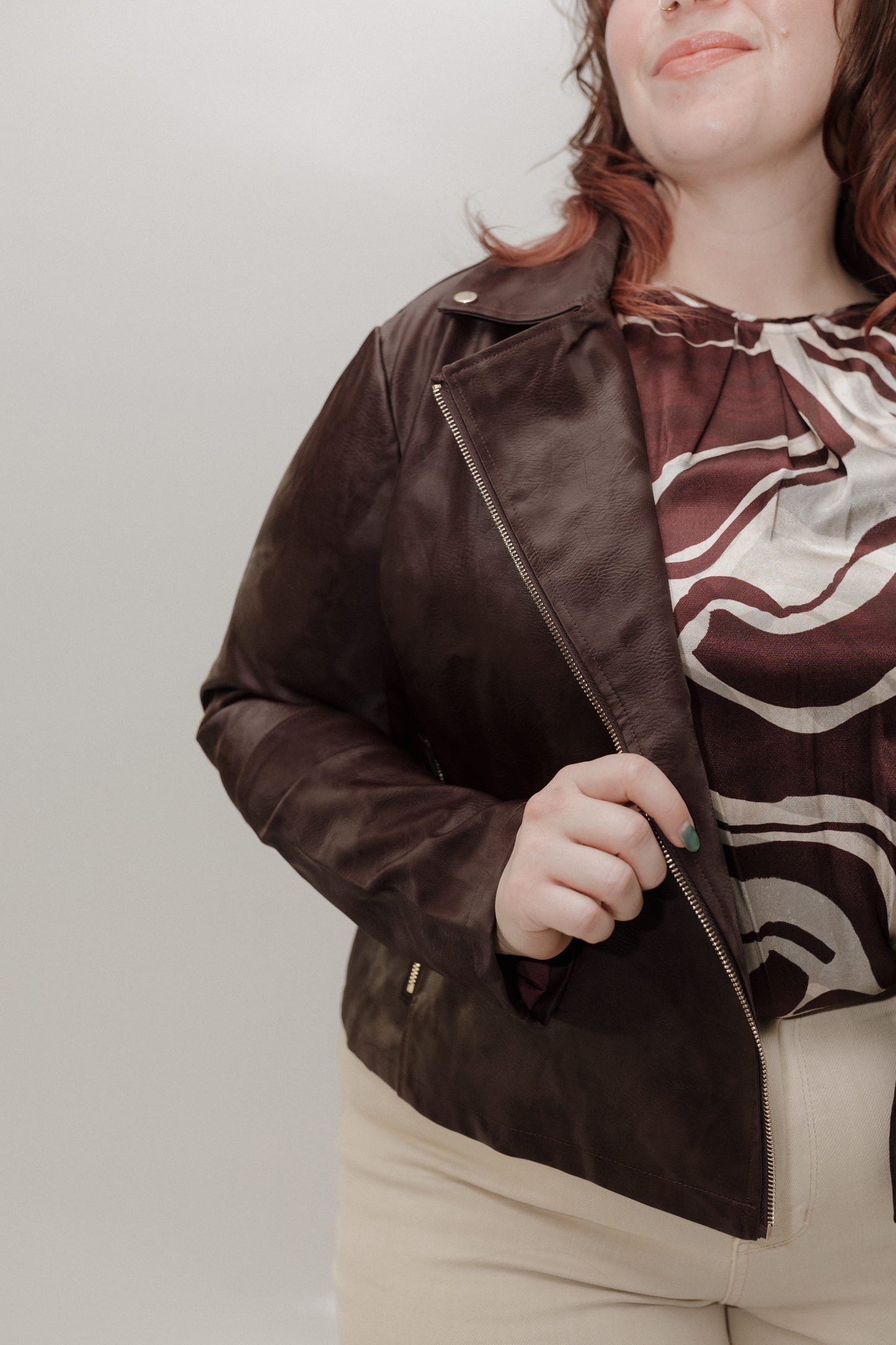 Person wearing a brown leather jacket with a patterned top against a plain background