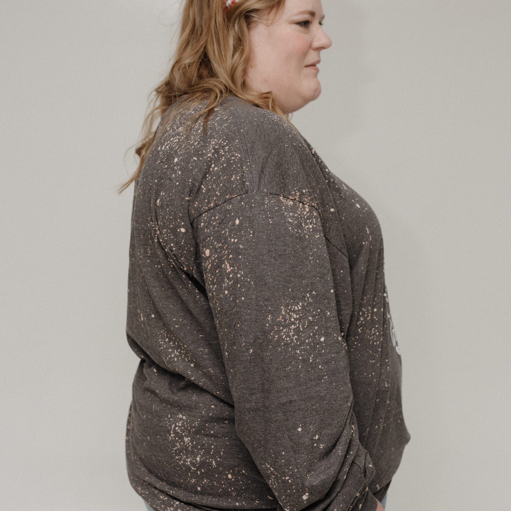 Woman wearing a sparkly gray sweater and blue jeans against a plain background